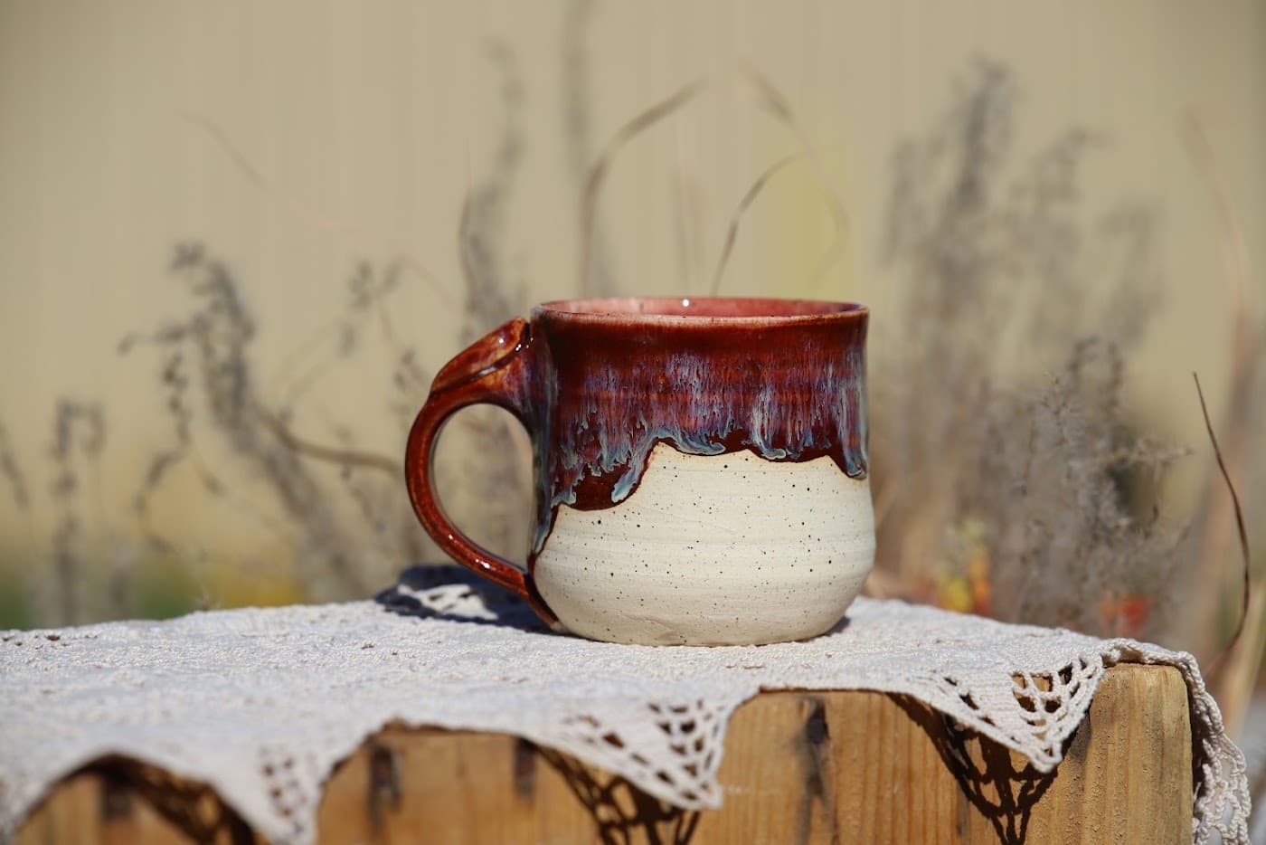 Speckled cream mug with dramatic oxblood and blue glaze dripping from a pink rim