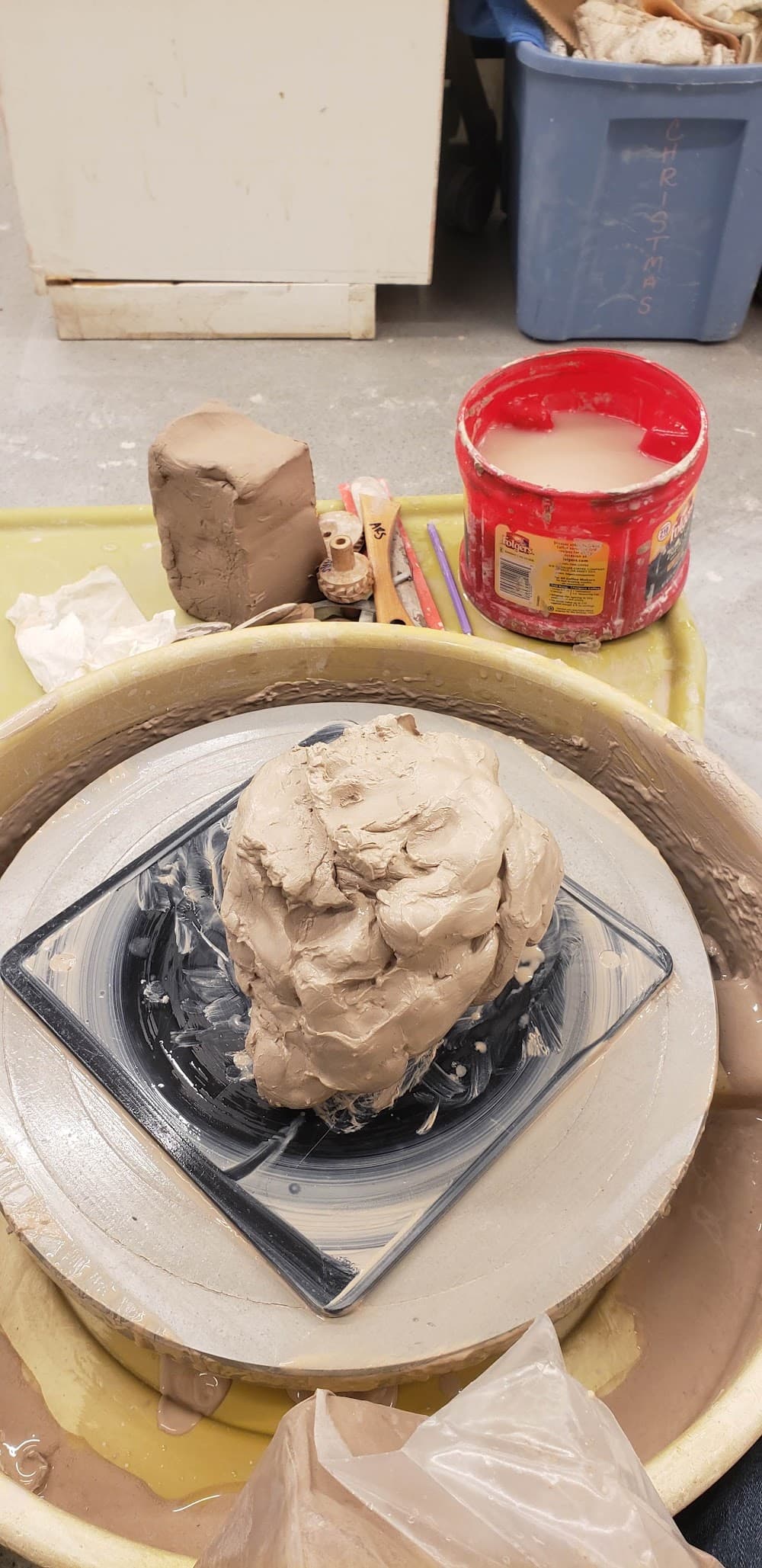 Lump of clay centered on the pottery wheel with tools and water bucket