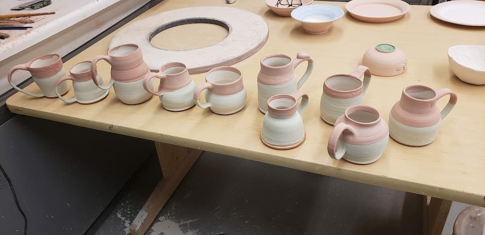 Glazed mugs lined up on a table before firing